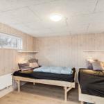 Two beds with wooden frames and bedding in a room with wooden walls and window.