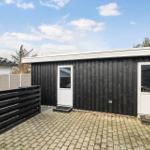 Black wooden shed with two white doors and paved outdoor area.