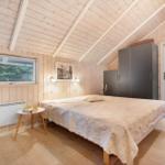 Bedroom with wooden walls, bed, wardrobe, and window with view of forest.