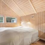 Bedroom with wooden walls and sloped ceiling, bed, windows, and desk.