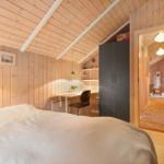 Bedroom with bed, desk, and wardrobe. Wooden walls and attic ceiling.