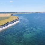View of coastal landscape with cliff, beach, and fields