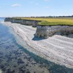 Steep cliff with beach and green fields on the horizon.