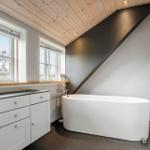 Badezimmer mit freistehender Badewanne, Holzdecke und Fenstern.