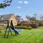 Haus mit Spielplatz, Trampolin und grünem Garten unter blauem Himmel.
