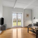 Wohnzimmer mit Sofa, Couchtisch und TV. Durchgang zur Küche. Fenster zur grünen Außenseite.