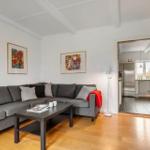 Wohnzimmer mit grauem Sofa, Holzboden und drei Wandbildern. Grüne Tür führt in die Küche.