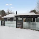 Black house with snow, glass fence, and tree background.