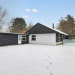 Black house with white facade, snow-covered garden and garage.