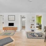 Living room with hardwood floor, TV, hallway, and view into home office with piano.