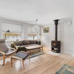 Living room with sofa, armchair, stove, and wooden floor.