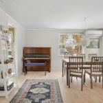A room with dining table, chairs, runner rug, and piano.
