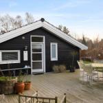 Black wooden house with white roof and terrace with table and chairs.