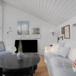 Living room with sofa, armchair, and round table. Posters hang on the wall, and a sailboat model stands by the window.
