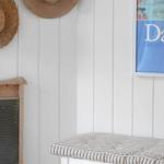 White seating area with striped cushion, straw hats and a picture on the wall.