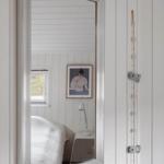 Mirror reflects bed, window, and wall art in white-paneled room.