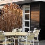 Deck with table and chairs in front of a wooden house with white windows.