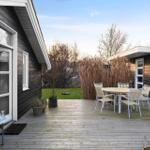 Deck with table and chairs in front of black wooden house with garden.