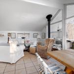 Living and dining area with wooden table, sofa, and seating. Large window front with view of outdoor area.