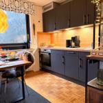 Küche mit Essbereich, Holzdielen und Fensterblick auf Bäume.