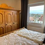 Schlafzimmer mit Holzschrank und Blick auf Wald und Häuser.