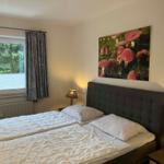 Schlafzimmer mit Doppelbett, Wandbild und Fenster mit Blick auf Wald.