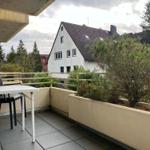 Balkon mit Tisch und Stühlen, Blick auf Wohnhaus und Bäume.