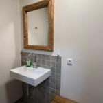 Badezimmer mit Waschbecken, Spiegel und Holzbank.