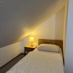 Ein Schlafzimmer mit Dachschrägen, Bett, Nachttisch und Lampe.