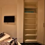 Schlafzimmer mit Bett, TV und Kleiderschrank mit Regalen.
