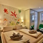 Schlafzimmer mit Bett, Wandmalerei und grüner Sitzgelegenheit.