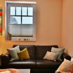 Schwarzes Ledersofa mit Kissen unter Fenster mit Jalousie.
