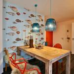 Essbereich mit Holztisch, bunten Stühlen und Fischmotiv-Wandtapete.