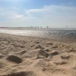 Beach with fine sand and people in the water at sunset.