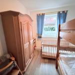 Room with crib, bunk bed, and wooden wardrobe. Window with blue curtains.