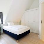 Bedroom with bed, wardrobe, and window. Wooden floor and sloped ceiling.