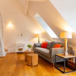 Wohnzimmer mit Sofa, Tischen und Holzboden unter Dachschrägen.