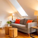 Wohnzimmer mit Sofa, Holztischen und Lampen unter Dachschrägen.