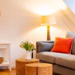 Ein Wohnzimmer mit grauem Sofa, orangefarbenem Kissen, Holztisch und Stehlampe.