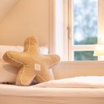 Schlafzimmer mit Bett, Sternkissen und Fenster.