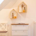 Weißer Schrank mit Holzoberfläche, daneben Stuhl und Wandregale mit Dekoration.