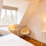 Schlafzimmer mit Dachschräge, Bett, Nachttisch, Stuhl und Fenster.