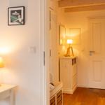 Flur mit Holzboden, weißen Wänden und einer Tür. Eine Lampe steht auf einem Schrank.