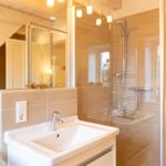 Bad mit Dusche, Waschbecken und Spiegel. Zwei Fische dekorieren den Spiegelrand.