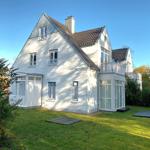 Weißes Haus mit Balkon und grünem Garten unter blauem Himmel.