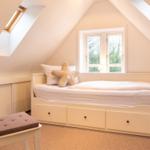 Ein Schlafzimmer mit Dachschräge, Fenster, Bett und Stuhl.