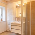 Badezimmer mit Dusche, Waschbecken und Fenster.