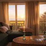 Wohnzimmer mit Sofa und Tisch. Durch Fenster ist Sonnenuntergang über Meer sichtbar.