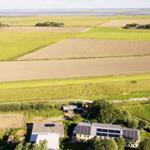 Haus mit Solaranlage in ländlicher Umgebung mit Feldern und Wasser.
