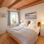 Schlafzimmer mit Holzboden, Bett und Fenster. Decke mit Holzbalken.